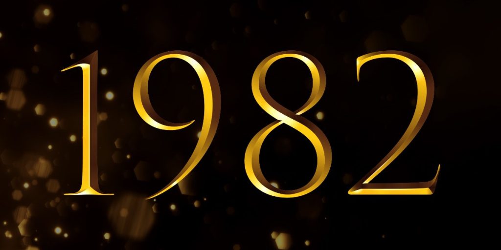 Golden text reading "1982" on a dark background with subtle light reflections and a festive atmosphere.