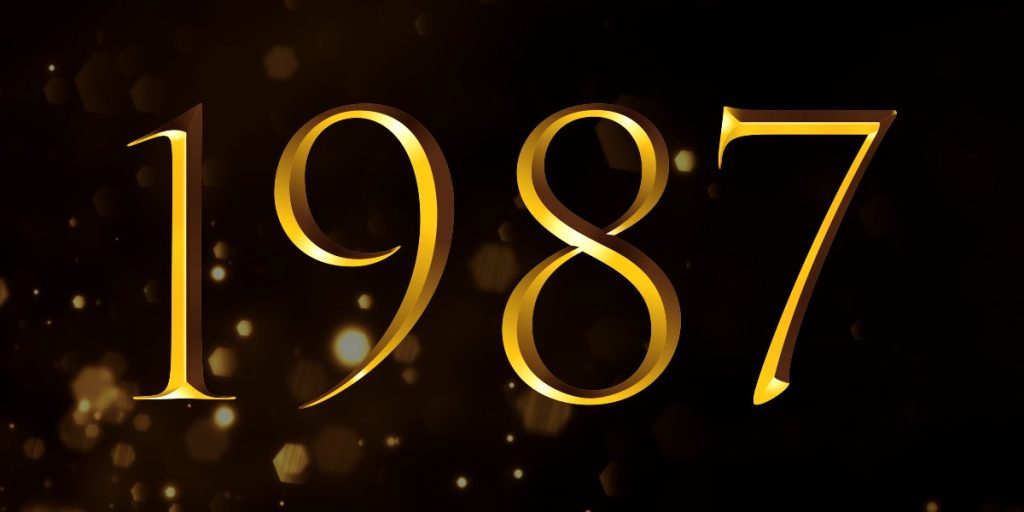 Golden numbers "1987" on a dark background with subtle light reflections and bokeh effects.