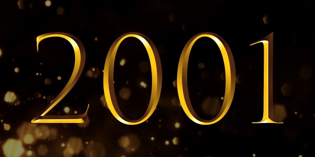 A woman in a formal black dress stands on stage, holding an award, with a spotlight illuminating her.