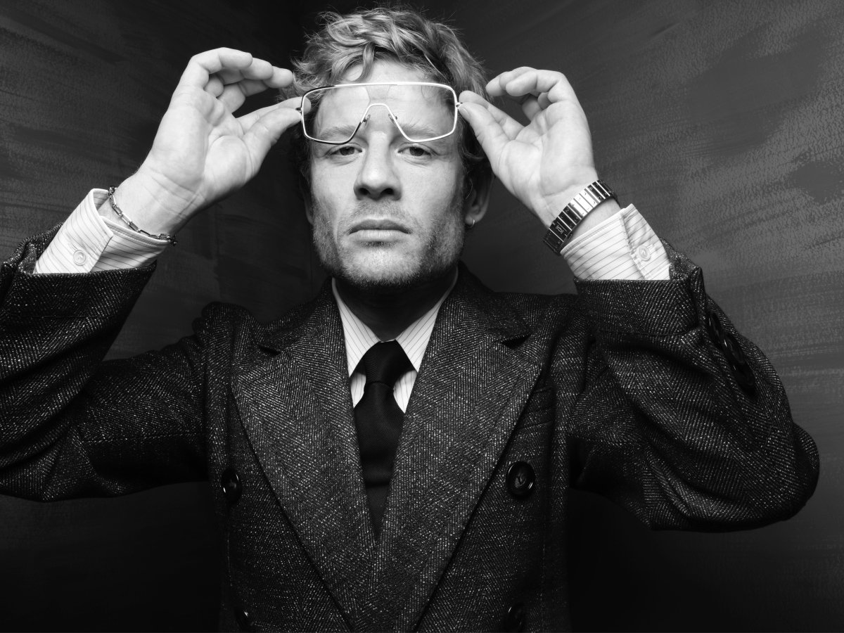 A man in a suit. He is wearing glasses which he is holding slightly off his face.