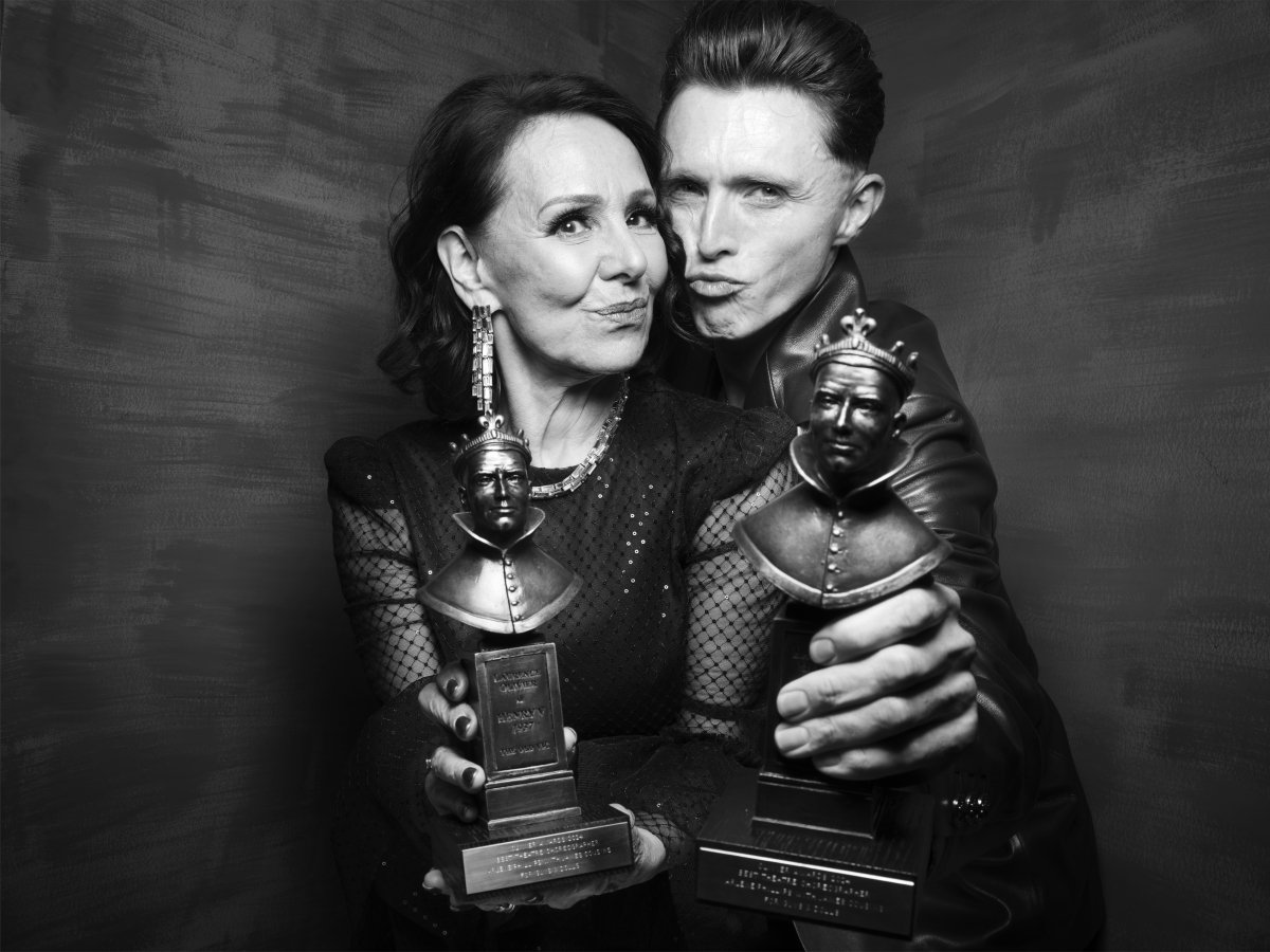A woman and man are cheek and pouting. They are holding their Olivier Award statues out in front of them.