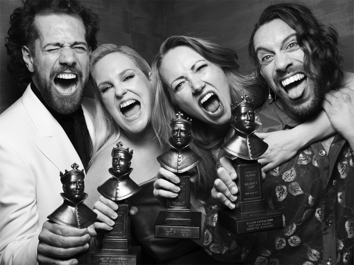 Four people smile widely at camera holding awards.