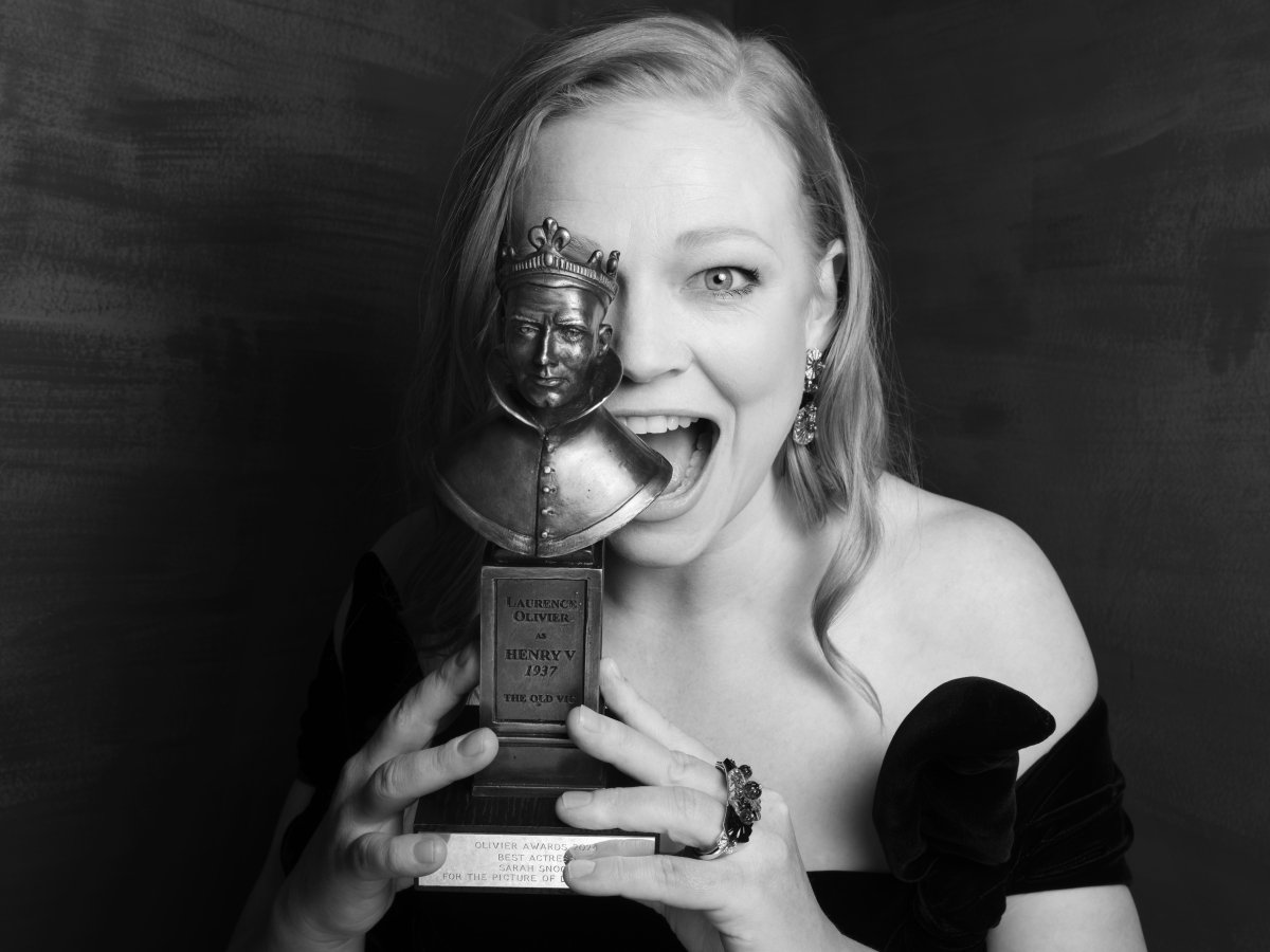 A black and white image of a person holding an award over half their face and smiling.