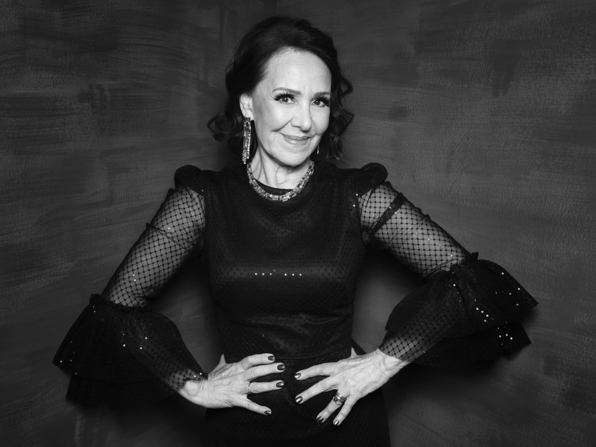 A woman in a dress smiling with her hands on her hips.