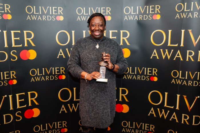 Vereen Irving holds her Olivier Award statuette in front of a branded backdrop