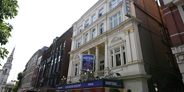 The Duke of York's Theatre exterior, featuring red brick walls and a clear blue sky background.